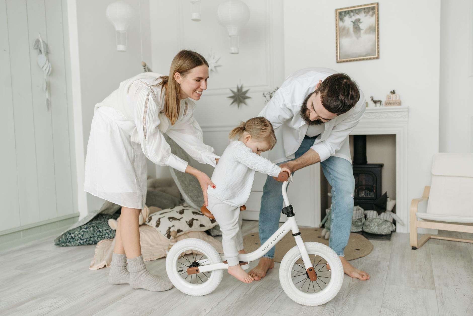 Rodzice uczą dziecko jeździć na rowerku biegowym w salonie
